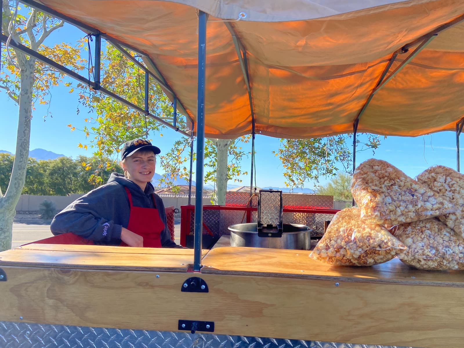 One of the Kettle Corn Bros smiling behind the cart, Tucson mountains behind